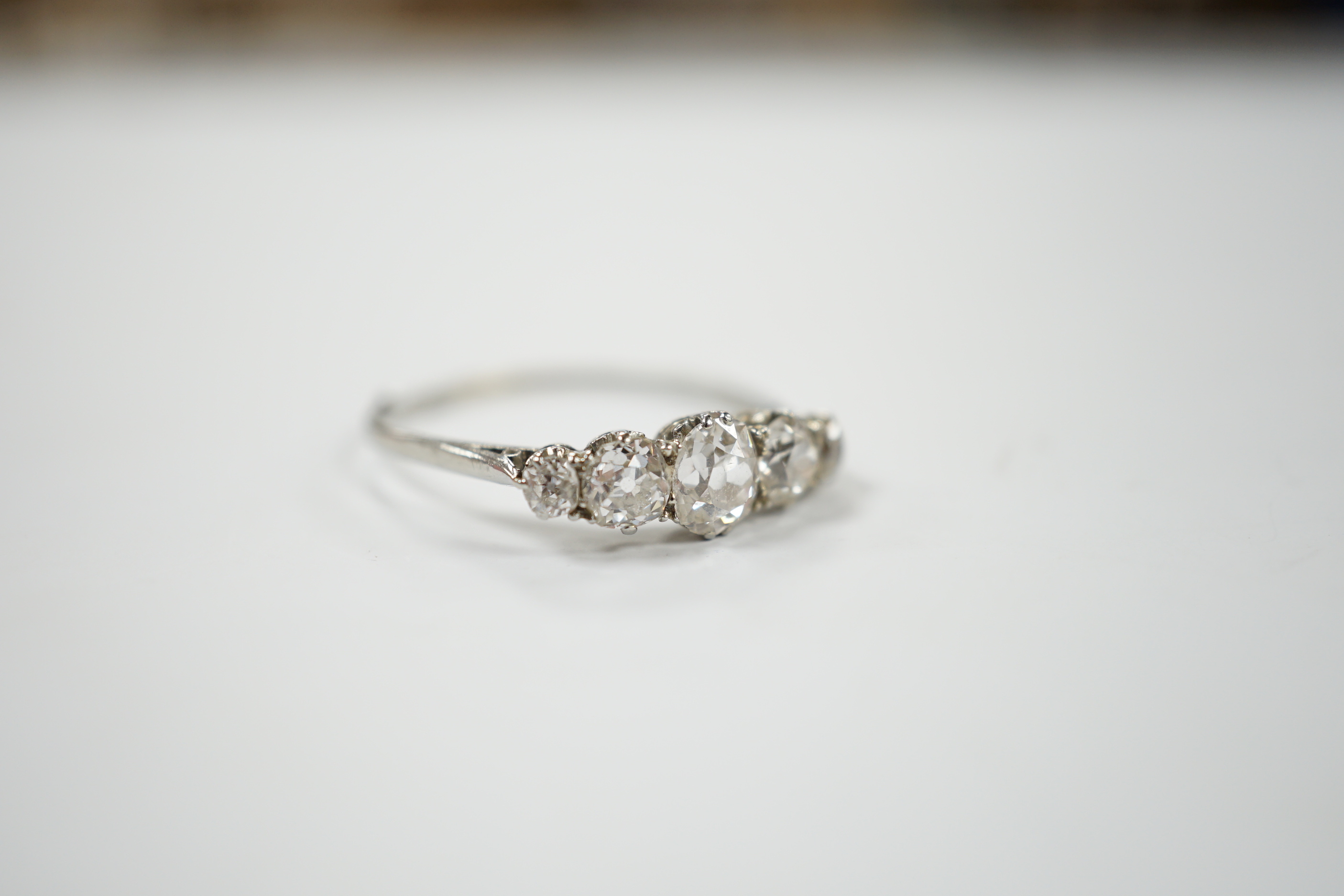 An 18ct white metal and graduated five stone diamond set half hoop ring, size X/Y, gross weight 2.2 grams.